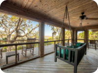 A porch swing overlooking trees and a green field.