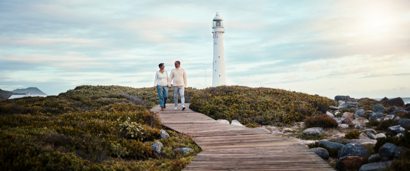 A couple holding hands on a boardwalk walking away from a lighthouse