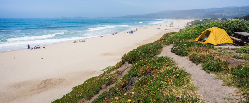 A tent camped on the coastal bluffs of the Pacific Ocean.