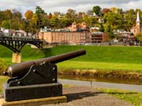 Historic cannon with a bridge and hilly city in the background