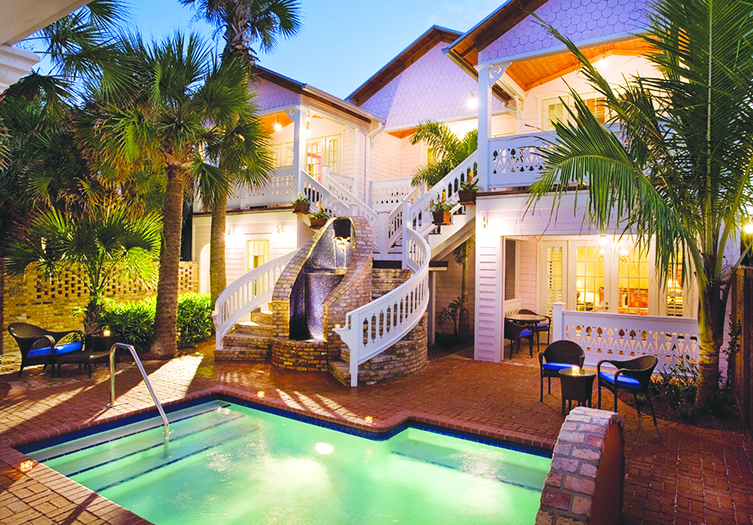 Courtyard view of Port d’Hiver Bed and Breakfast with a small illuminated pool, curved staircase, palm trees, and cozy seating area at dusk.